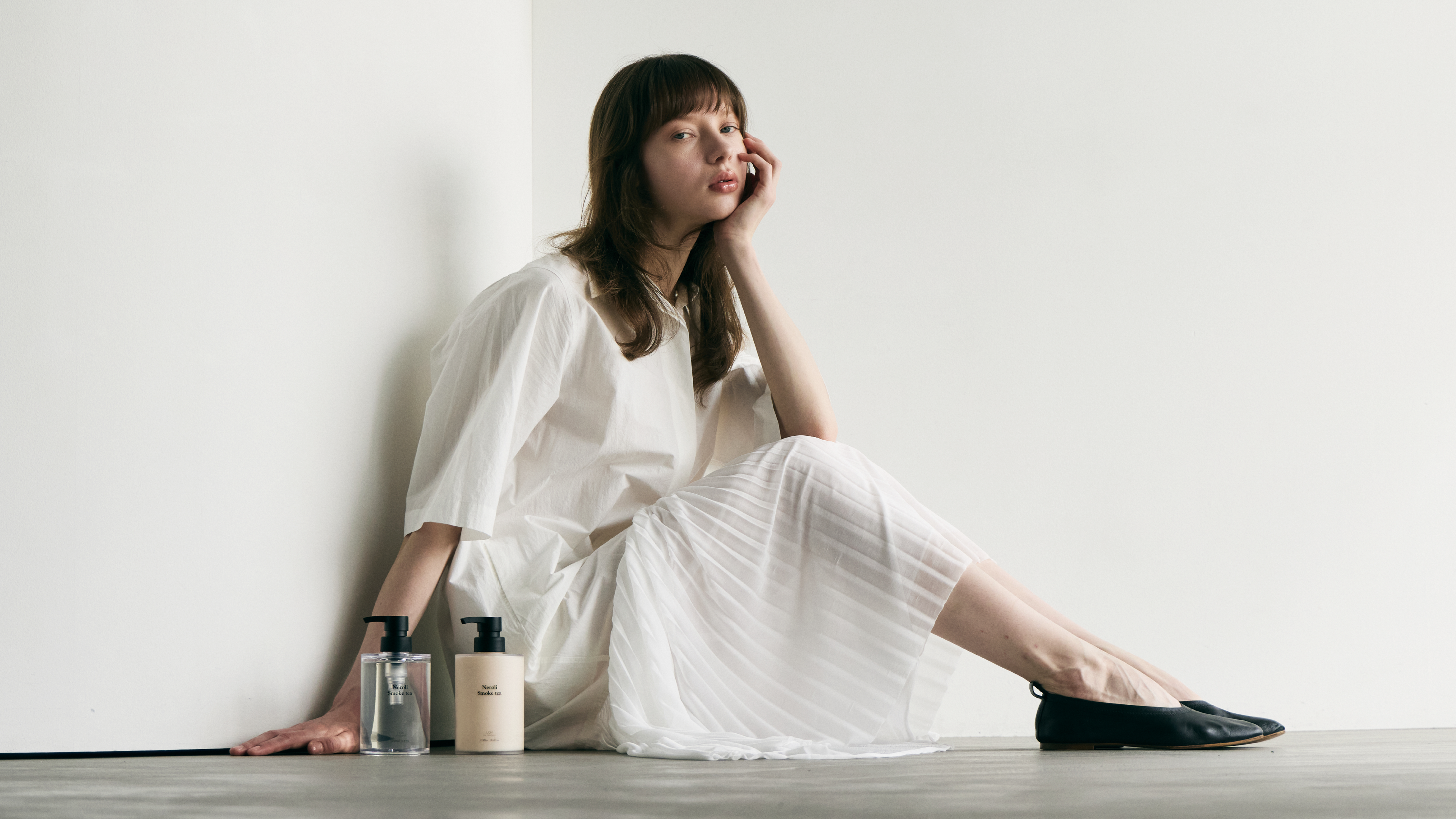 LOA THE SHAMPOO TREATMENTの商品が2つ床に置いてある後ろに女性が座って膝に肘をついてポーズをしている